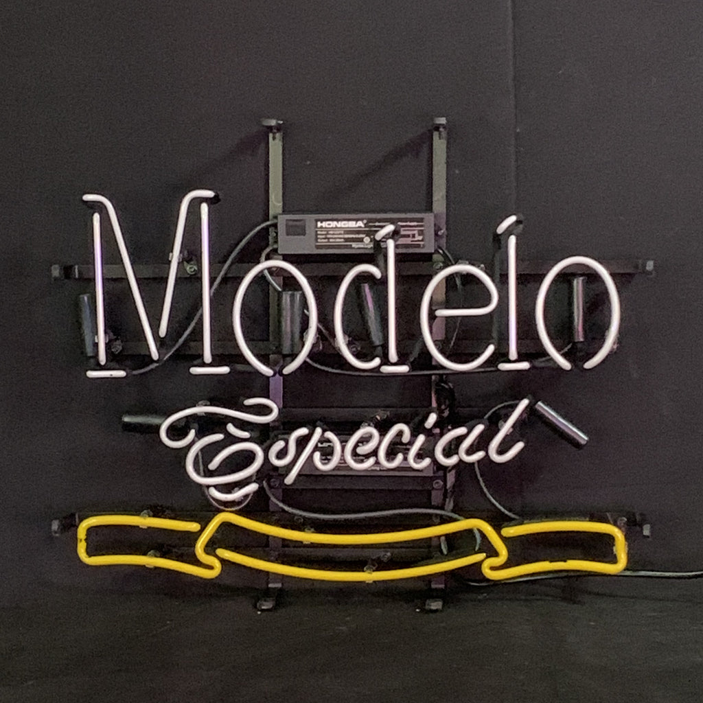 White and yellow neon sign reading 'Modelo Especial' with script and block lettering on a black background, mounted on a black metal frame with power unit.
