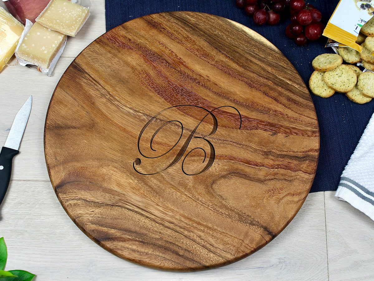 Medium round wooden charcuterie board with a dark engraved script letter B in the center, showing natural wood grain patterns and warm brown tones.