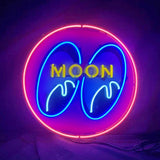 Circular neon sign with pink outer ring, blue stylized eyes inside, and yellow uppercase letters spelling MOON across the eyes on a dark background.