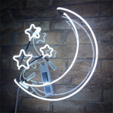 White neon light shaped as a crescent moon with three stars, mounted on a clear backing against a brown brick wall, with wiring and components visible.