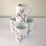 Set of four white ceramic mugs decorated with brown branch and bird silhouettes, one stacked atop the others, showing two birds perched closely on a branch design.
