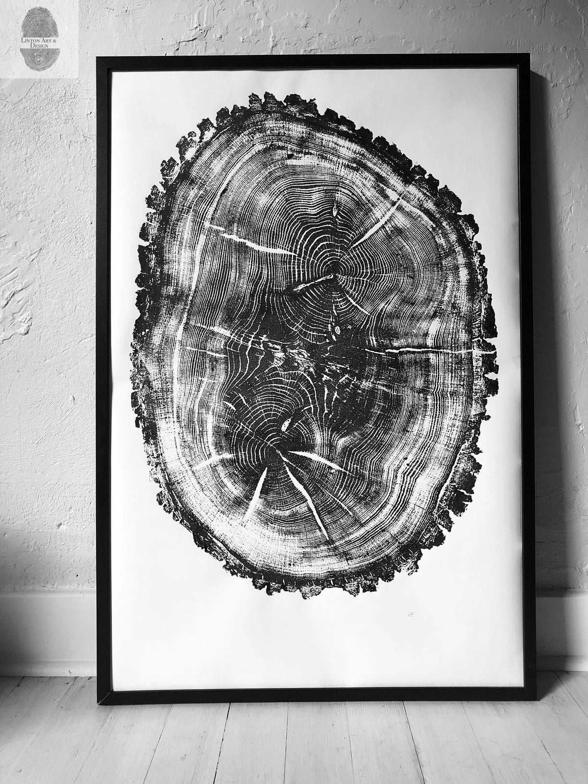 Black-and-white framed print of an oak tree cross-section showing detailed growth rings and bark texture, leaning against a textured white wall on a light wood floor.