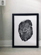 Black and white framed print of a detailed cross-section of a tree trunk showing annual rings and texture, leaning against a light textured wall on a pale wooden floor.
