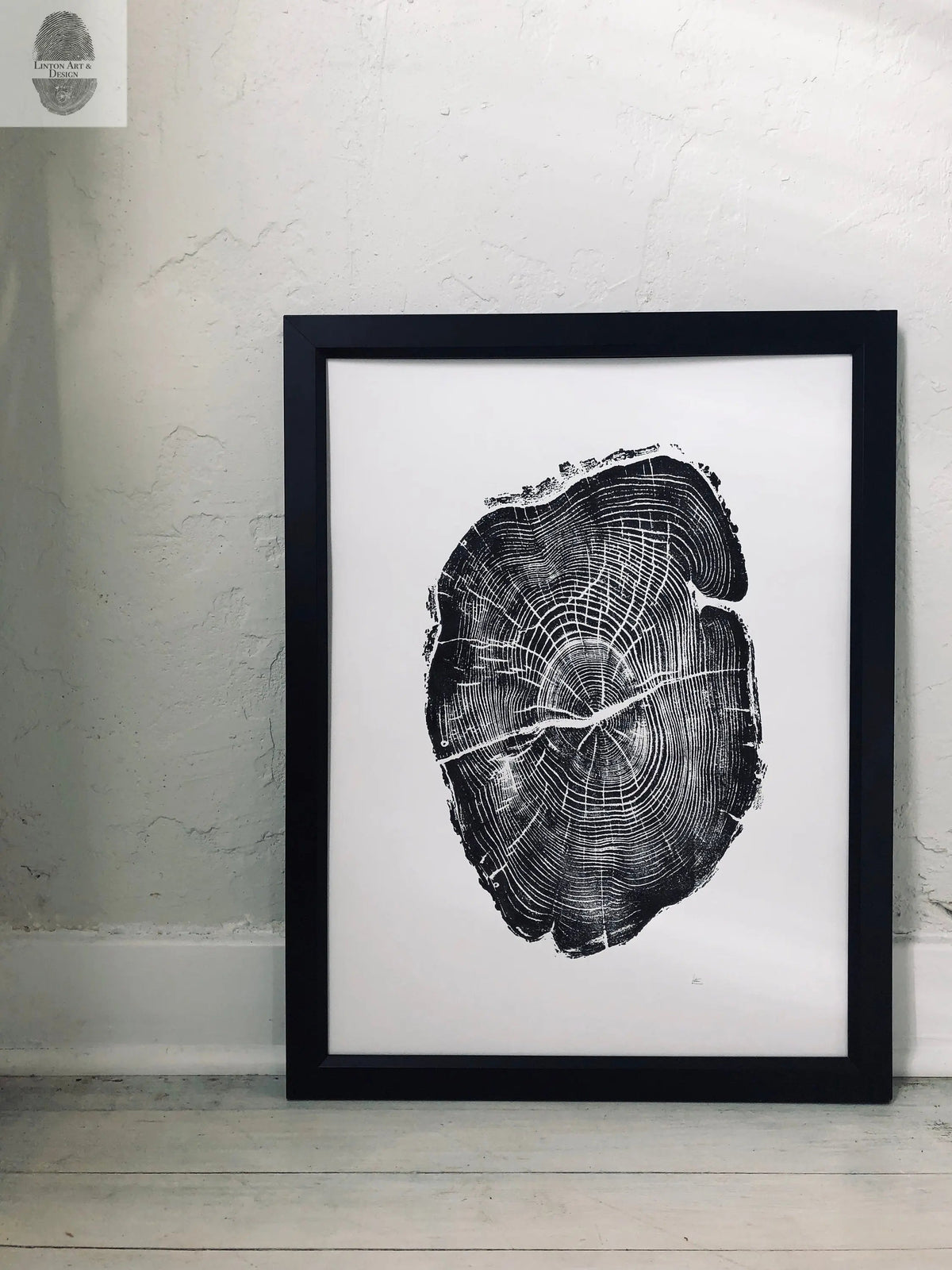Black and white framed print of a detailed cross-section of a tree trunk showing annual rings and texture, leaning against a light textured wall on a pale wooden floor.