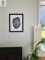 Black and white framed print of a tree cross-section with visible rings hanging on a textured off-white wall above a dark wooden cabinet, near a window with shutters and green plants.