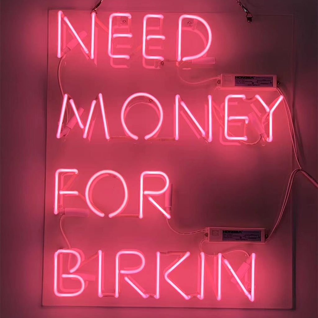 Bright pink 'Need Money for Birkin' neon sign illuminated against a neutral background