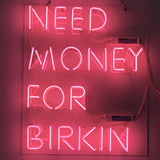 Bright pink 'Need Money for Birkin' neon sign illuminated against a neutral background