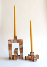 Two geometric candle holders with beige, brown, and white abstract patterns, one square frame with a rectangular candle and one cross-shaped base with a tapered candle