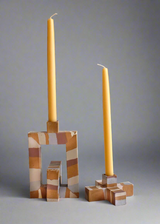 Two square-patterned candle holders with beige, white, and brown stripes, holding tall yellow taper candles against a gray background.