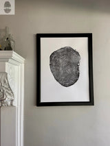Black framed print of an ash tree cross-section with detailed rings and texture, hanging on a light-colored wall near a white ornate fireplace with glass bottles on top.