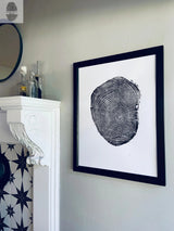 Black and white framed print of detailed ash tree rings, hung on a pale gray wall beside a white mantel with star-patterned tile and glass bottles on top.