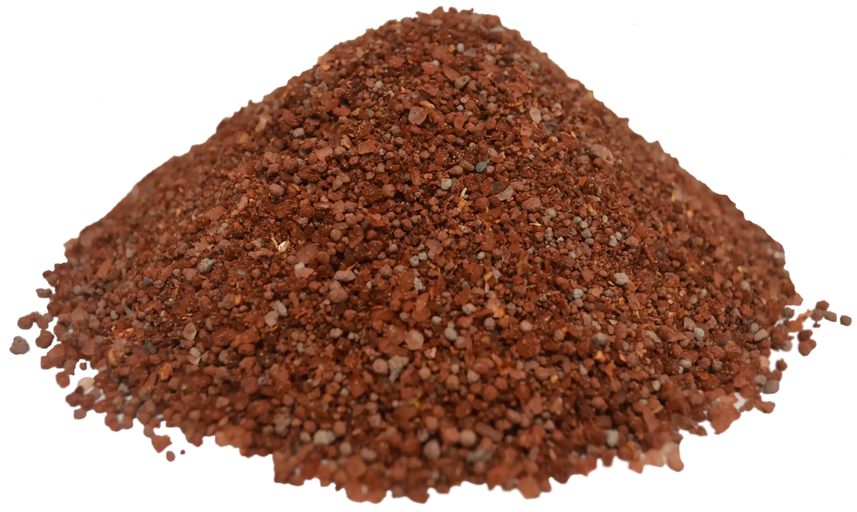 Pile of reddish-brown granular mineral and vitamin supplement with uneven small particle sizes on a white background.
