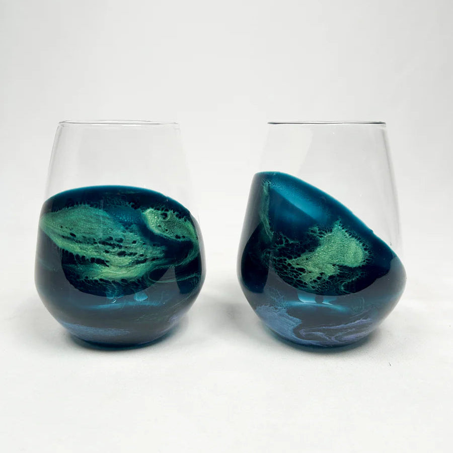 Two stemless wine glasses with blue and green resin marbled design on a white background