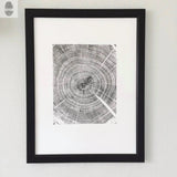 Black and white detailed print of an oak tree cross-section showing tree rings, framed in a simple black frame against a white wall.