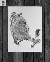 Black ink print of a weathered tree ring cross-section with irregular bark edges on white paper, placed on dark wooden floorboards.