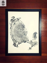 Black and white tree ring print in a black frame, showing detailed wood grain patterns on a white background against wooden floorboards.