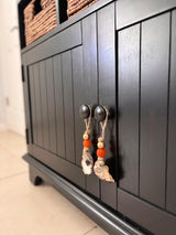 Black paneled cabinet doors with round black knobs, each adorned with rustic string ornaments featuring natural seashells and orange wooden beads.