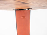 Detail of a curved wood desk edge mounted on a smooth brown leather panel with stitched sides and an embossed circular logo on a white background.