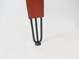 Close-up of black metal hairpin-style desk leg supporting a brown leather-covered corner on a white background.