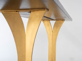 Black sofa table with paired gold split legs curving gracefully from tabletop to floor, shown from a low side angle against a white background.