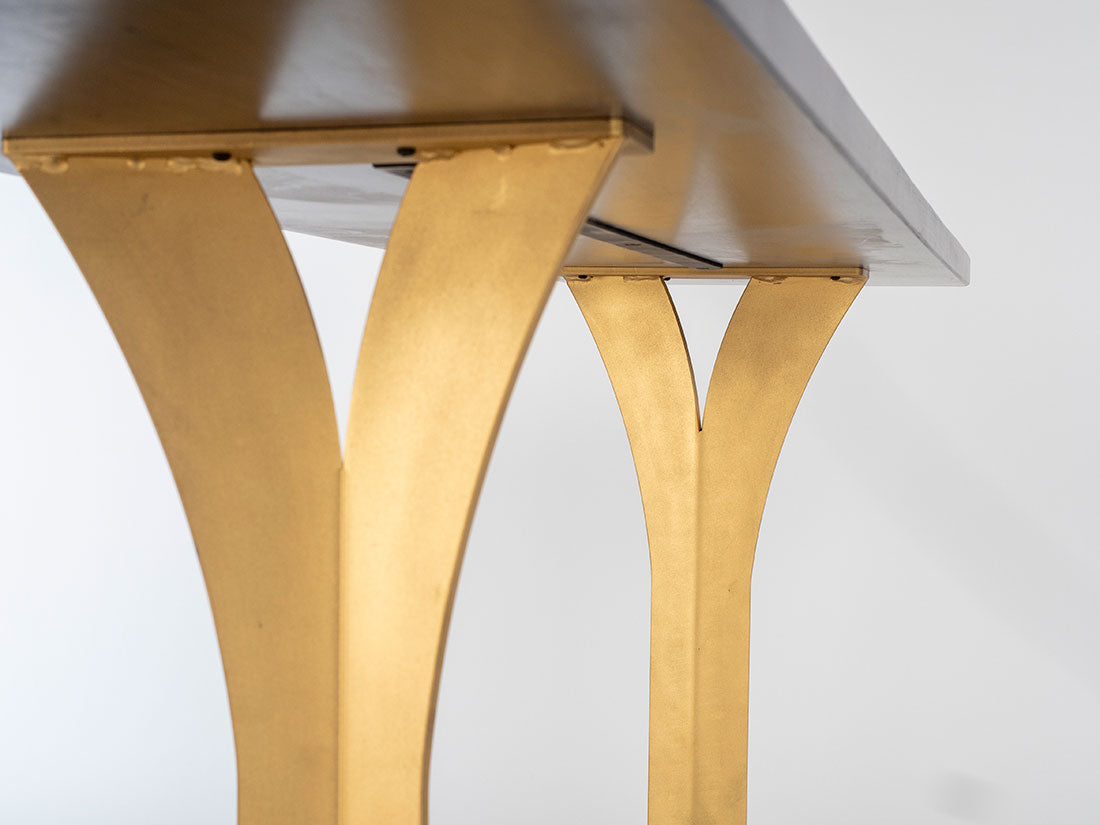 Black sofa table with paired gold split legs curving gracefully from tabletop to floor, shown from a low side angle against a white background.