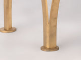 Close-up of gold-toned metal bench legs with a split design, featuring a textured surface and circular base plates on a white floor.