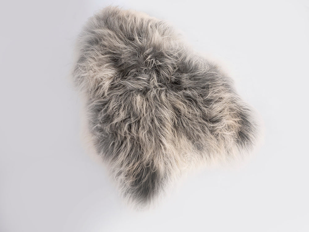Irregularly shaped soft Icelandic sheepskin rug with long, fluffy fur in shades of grey and white on a light background.