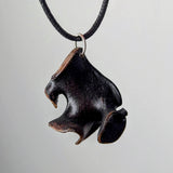 Black irregularly shaped pendant with smooth wave-like edges and subtle brown highlights, hanging on a black cord with a silver ring against a gray background.
