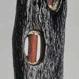 Close-up of a textured dark wooden pendant with an elongated oval cutout revealing a smooth reddish-brown inner piece, highlighting natural wood grain contrasts.