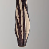 Close-up of a pendant with a twisted organic shape featuring dark brown textured grooves contrasting against smooth beige surfaces, hanging against a neutral background.