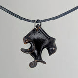Dark wood pendant shaped like an abstract, angular bird head with a curved beak, suspended on a thin black braided cord with silver metal ring.