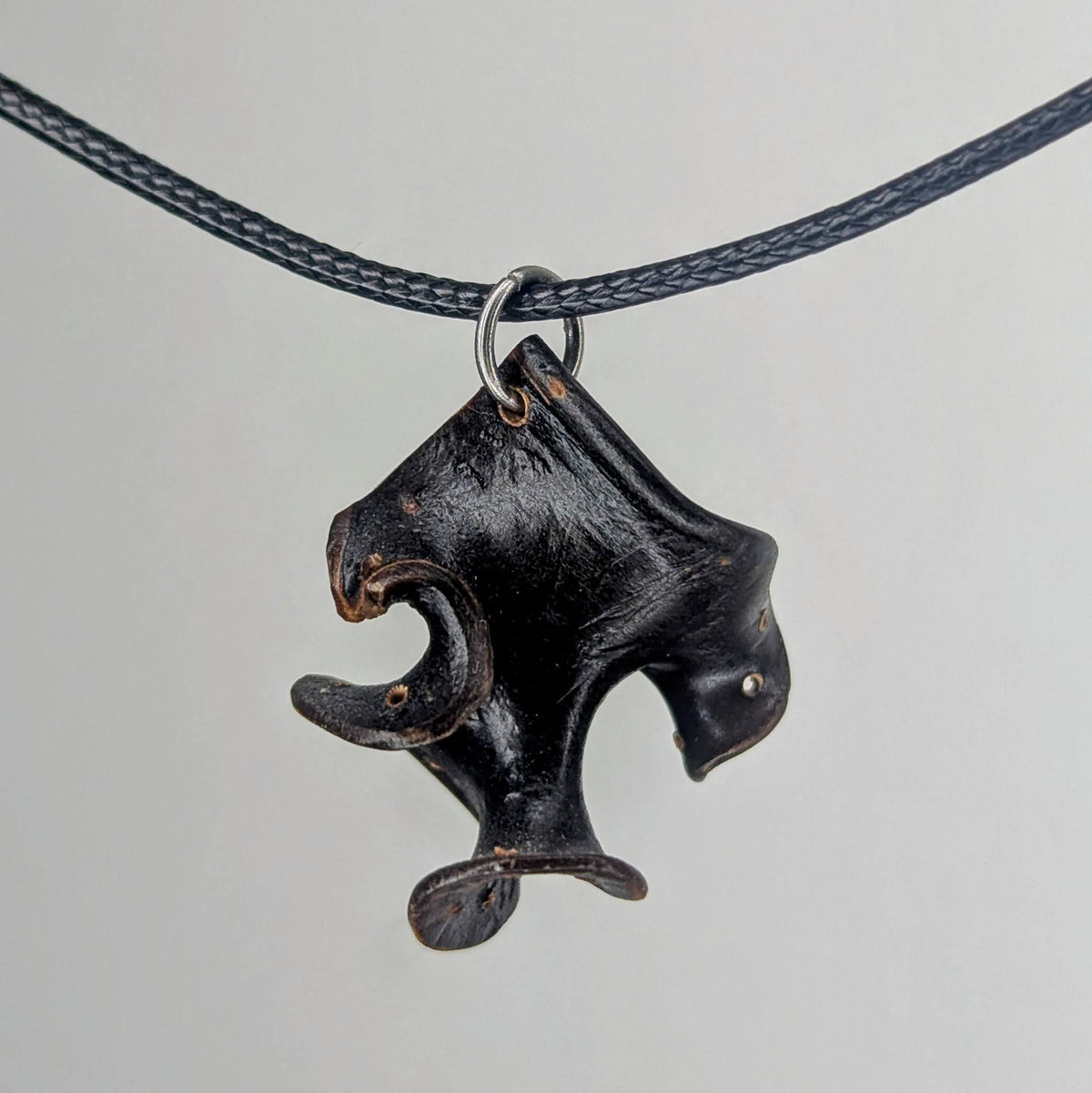 Dark wood pendant shaped like an abstract, angular bird head with a curved beak, suspended on a thin black braided cord with silver metal ring.