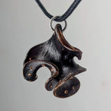 Dark brown pendant shaped like an abstract curled fungus or flower with small round indentations, suspended on a black cord with a silver ring.