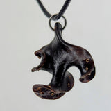 Dark, abstract wooden pendant with a curved, organic shape and small circular inlays, suspended on a black cord against a light background.