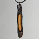 Dark textured pendant with an elongated amber center, hanging from a black cord against a plain gray background.