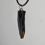 Black textured wooden pendant with a natural grain detail revealing a brownish streak, hanging from a black braided cord against a neutral background.