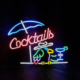 Neon sign featuring a blue umbrella above red script reading 'Cocktails' with a green parrot holding a yellow drink glass beside a blue cocktail glass on a black background.