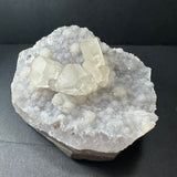 Cluster of translucent calcite crystals growing on a bed of white druzy quartz on an irregularly shaped agate base, displayed on a black surface.
