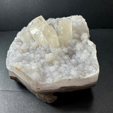 Clear druzy calcite crystal cluster with hexagonal prisms atop a sparkling white agate base with a rough bottom edge against a dark background