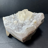 White druzy calcite crystal cluster with translucent rectangular crystals atop sparkling granular base on a dark background.