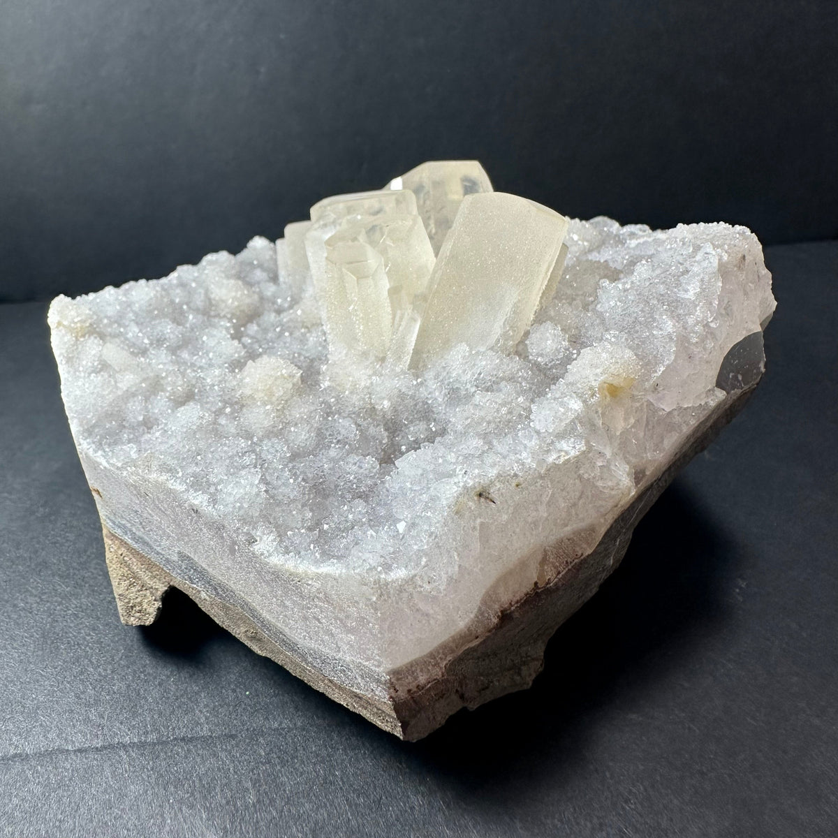 White druzy calcite crystal cluster with translucent rectangular crystals atop sparkling granular base on a dark background.