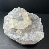 Close-up of Druzy Calcite cluster on a polished agate base with natural mineral textures visible, photographed on a neutral surface.