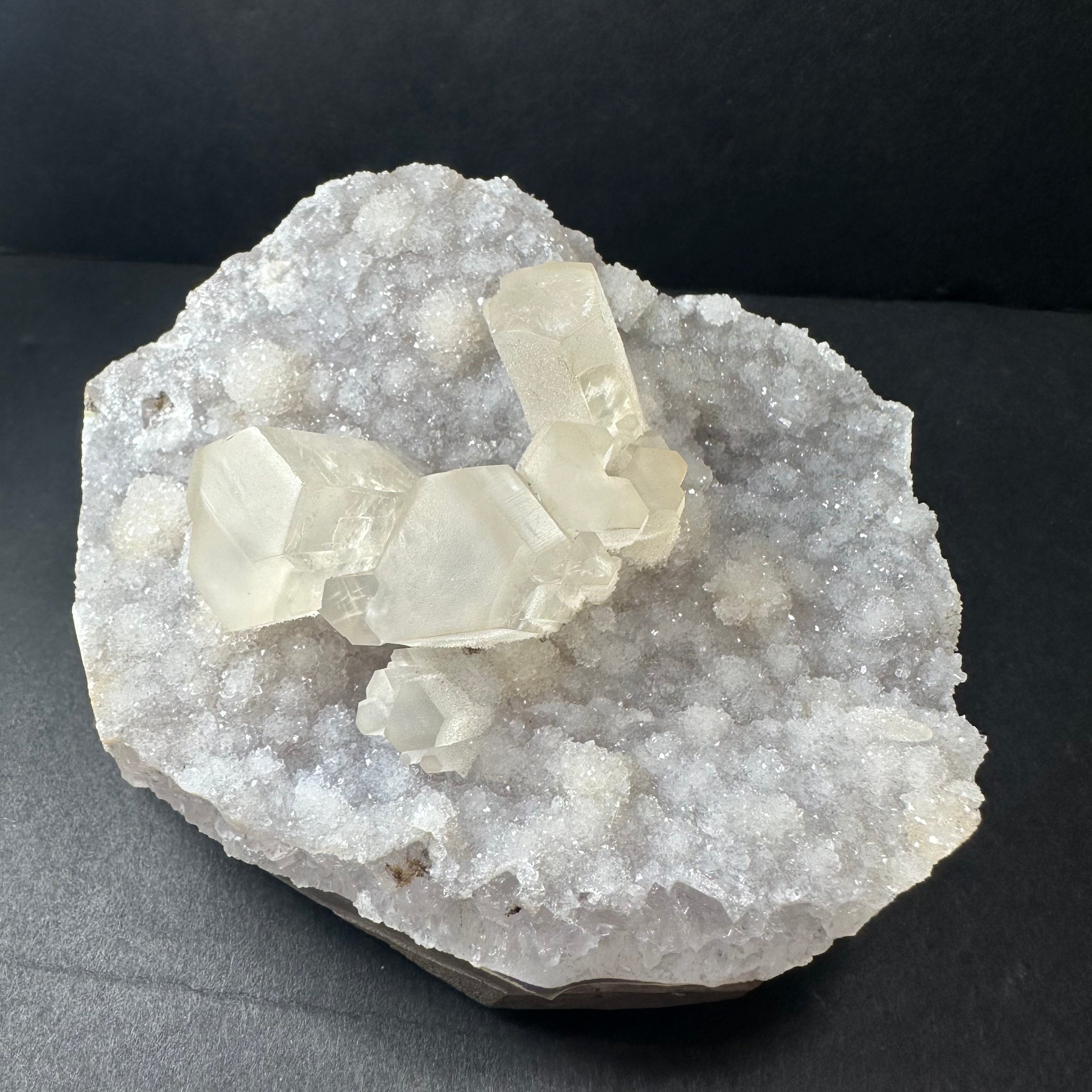 Close-up of Druzy Calcite cluster on a polished agate base with natural mineral textures visible, photographed on a neutral surface.