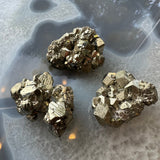 Three clusters of metallic cubic pyrite crystals with shiny gold color and geometric facets, displayed on a translucent, quartz-like surface with natural patterns.