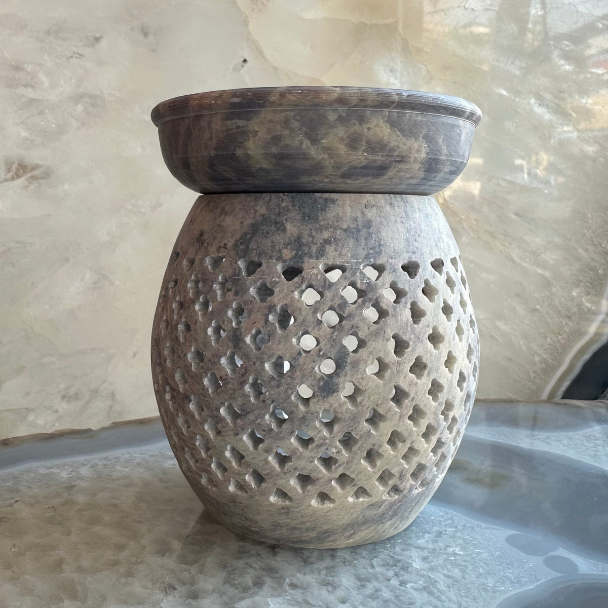 Round soapstone essential oil burner with latticework pattern and a shallow bowl on top, showing natural gray and beige marbled stone texture.