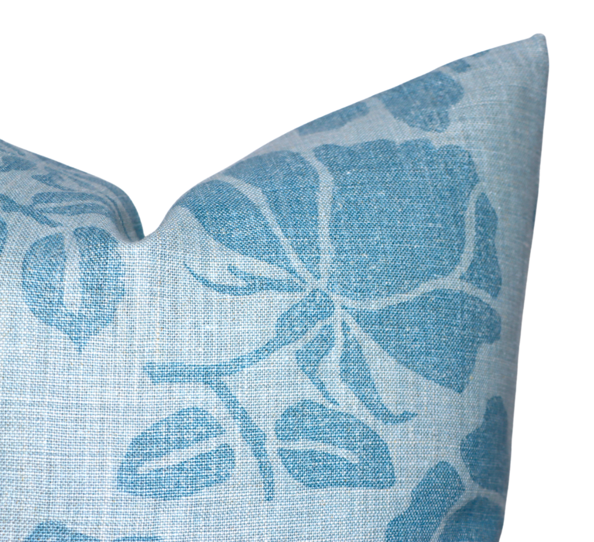 Close-up of a pillow corner featuring a blue floral pattern with large stylized petals and leaves on textured light blue fabric.