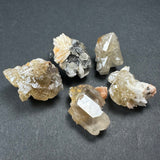 Five translucent beige and white mineral specimens with crystalline structures, some with white and black matrix, displayed on a dark gray background.
