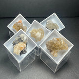 Five mineral specimens with translucent and crystalline formations in white display trays set on clear acrylic boxes against a dark background.