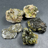 Five mineral specimens with green, gold, and dark crystalline formations on gray background, showing varied textures and reflective surfaces.
