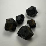Five small black cubic and octahedral mineral specimens with a slightly reflective surface arranged on a plain white background.